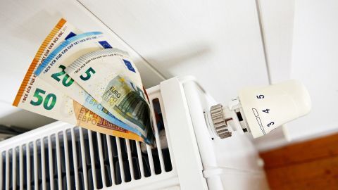 Ein Heizkörper mit Geldscheinen steckt in den Lamellen, was auf das Thema Heizkosten sparen hinweist.