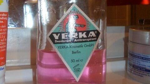 Yerka gegen Schweiß: Effektiver Schutz vor Achselnässe, einfach aufgetragen. Das sichtbare Spray in der Abbildung zeigt die typisch rosa Flüssigkeit in der 50 ml Flasche, die diskret im Badschrank stehen kann. Eine Yerka-Flasche steht auf einem Badezimmertisch neben Kosmetik, enthält pinke Flüssigkeit und trägt das Etikett "Yerka Kosmetik GmbH Berlin 50 ml".