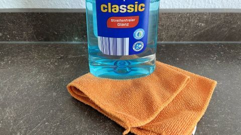 Klarspüler ist ein effektives Hausmittel, um Flecken von Sofas, Polstermöbeln und Teppichen zu entfernen: Man sollte dabei ein fusselfreies und farbechtes Tuch verwenden. Ein Flasche Klarspüler steht auf einem orangefarbenen Tuch, bereit, um Flecken von Polstermöbeln und Teppichen zu entfernen.
