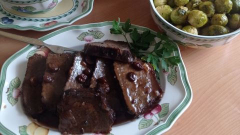 Zartes Sauerbraten liegt in einer Umami-Soße, umgeben von Spätzle und Rosenkohl auf einem gedeckten Tisch.