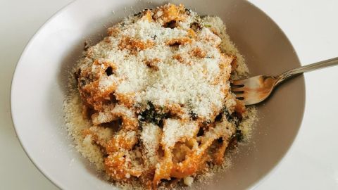 Ein Teller Pasta mit selbstgemachter Tomatensoße und Blattspinat, bedeckt mit Parmesan, steht auf einem Tisch.