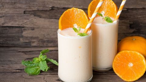 Zwei Gläser mit cremigem Getränk, garniert mit Orangenscheiben und Minze, stehen auf rustikalem Holz.