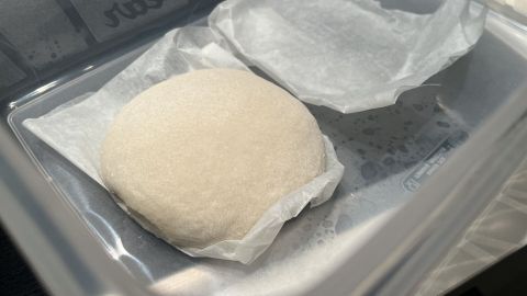 Ein runder Pizzateigling liegt auf Pergamentpapier in einem transparenten Behälter, bereit zum Einfrieren.
