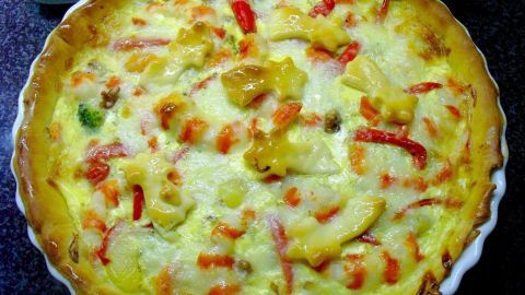 Eine farbenfrohe Quiche mit Lachs, Surimi und Käse, frisch gebacken und appetitlich auf einem weißen Teller serviert.