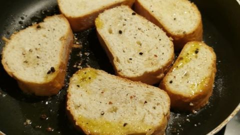 In einer Pfanne braten mehrere Scheiben altes Brot mit Gewürzen und Öl, um eine knusprige Textur zu erreichen.