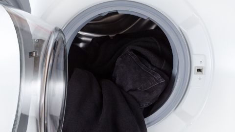 Schwarze Wäsche liegt in einer Waschmaschine, die Tür ist geöffnet und zeigt die dunklen Kleidungsstücke im Innenraum.