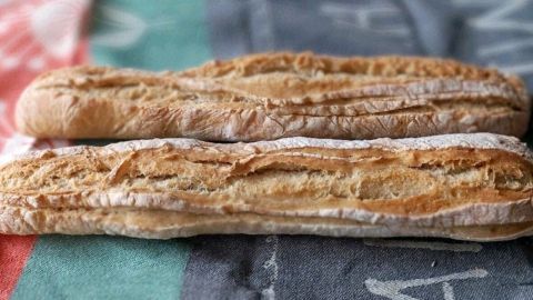 Zwei frisch gebackene Dinkelbaguettes liegen auf einem bunten Geschirrtuch und warten darauf, serviert zu werden.