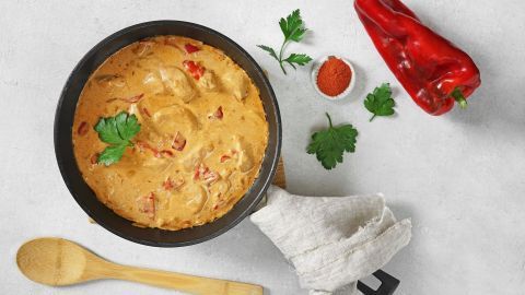 Saftige Hühnerbrust schwimmt in einer cremigen Paprikasoße, umgeben von frischen Kräutern und einer Paprika.