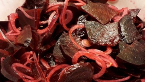 Rote Bete-Salat liegt in einer weißen Schüssel, aus geschnittenen roten Rüben und Zwiebelringen bestehend.