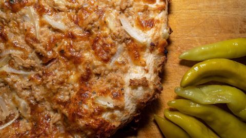Eine knusprige Pizza liegt auf einem Holzbrett, daneben frische grüne Peperoni, bereit zum Servieren.