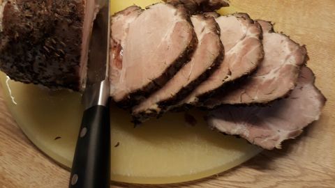 Saftiger Schweinebraten wird auf einem schneidenden Brett in gleichmäßige Scheiben geschnitten, umgeben von einer Holzoberfläche.