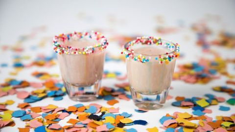 Zwei kleine Gläser mit buntem Zuckerrand stehen auf einer bunten Konfettiauflage, die eine festliche Stimmung schafft.