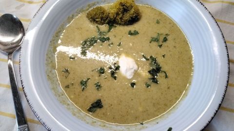 Eine cremige Brokkoli-Suppe mit Kartoffeln, garniert mit frischen Kräutern und einem Klecks Sahne, serviert in einer Schüssel.