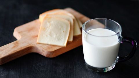Ein Glas Milch steht neben Scheiben Käse auf einem Holzbrett, was auf die Herausforderungen bei Laktoseintoleranz hindeutet.