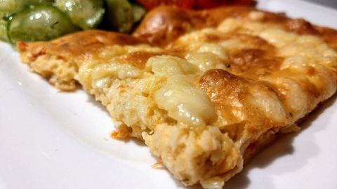 Eine krosse Schüttelpizza liegt auf einem weißen Teller, während frisches Gemüse daneben angerichtet ist.