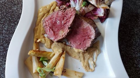 Saftiges Rinderfilet liegt auf einem weißen Teller, umgeben von gebratenem Spargel und einer cremigen Sauce.