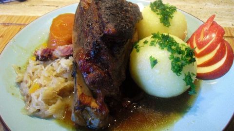 Saftiges Schäufele liegt auf einem Teller, umgeben von Knödeln, Sauerkraut und einer dunklen Biersoße.