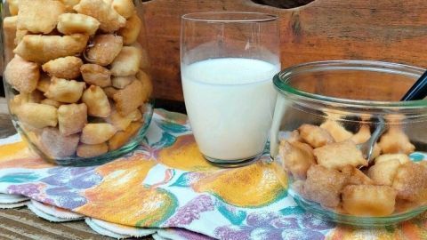 Zimt-Ministücke sind in einem Glas und einer Schale platziert, neben einem Glas Milch auf einem bunten Tuch.