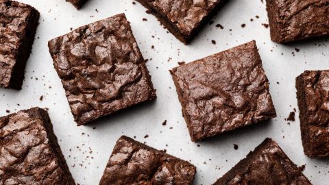 Saftige Brownies liegen auf einem Backpapier, gleichmäßig verteilt, und zeigen ihre schokoladige Oberfläche mit einer leicht glatten Textur.