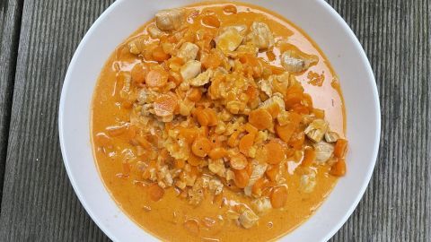 Hähnchenstücke in einer cremigen Sherry-Aprikosen-Sauce mit Karotten, serviert in einer weißen Schüssel auf Holz.