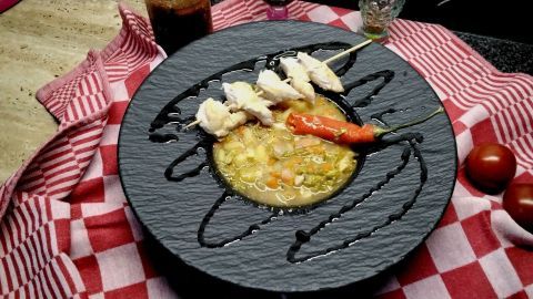 Eine schmackhafte Gemüsesuppe mit zarten Hähnchenspießen wird kunstvoll auf einem schwarzen Teller angerichtet.