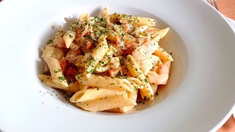 Penne wird mit Garnelen in einer cremigen Sauce serviert und ist auf einem weißen Teller in einem hellen Raum angerichtet.
