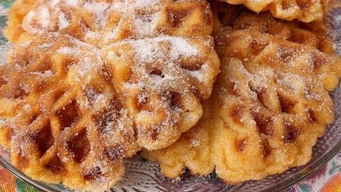 Goldbraune Churros-Waffeln liegen auf einem dekorativen Teller, bestreut mit Puderzucker, appetitlich angerichtet.
