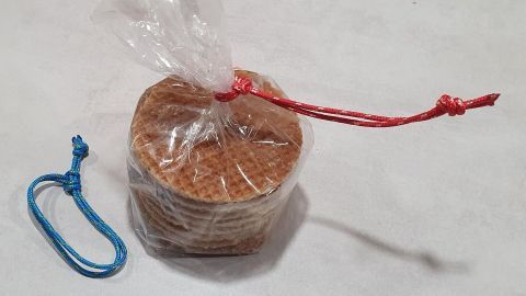 Ein Bündel Waffeln ist in einer durchsichtigen Folie verpackt, mit einem roten Knoten gesichert, während ein blauer Schlaufe daneben liegt.