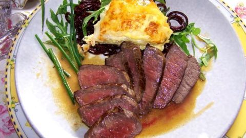Saftige Rinderfilet-Scheiben liegen auf einem Teller neben Kohlrabi-Gratin und frischem Grün, appetitlich angerichtet.