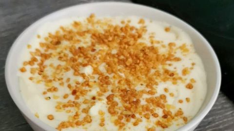 Eine cremige No-Bake Cheesecake-Variante in einer Schüssel, garniert mit einer knusprigen Keksstreuseln, steht auf einem Holztisch.