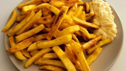 Ein großer Teller mit knusprigen Pommes frites befindet sich auf einem Tisch, daneben liegt eine Portion Mayonnaise.
