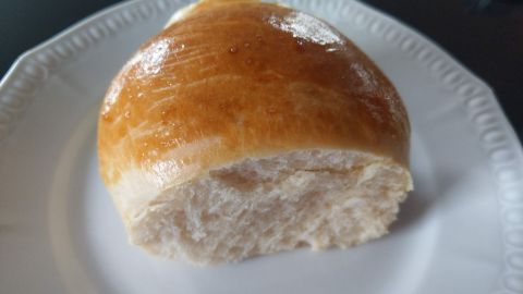 Ein frisch gebackenes Brötchen liegt auf einem weißen Teller und zeigt eine goldene, glänzende Kruste.