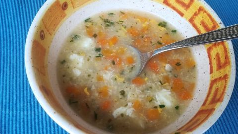 Eine Schüssel mit Hafer-Kraftsuppe, gefüllt mit Karottenstücke und Ei, steht auf einem blauen Tischmitteldecke.