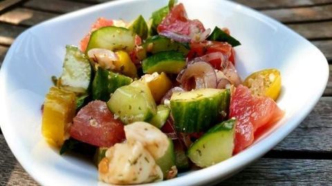 Ein bunter Tomatensalat mit Mozzarella und Gurke wird in einer weißen Schale präsentiert und zeichnet sich durch frische, knackige Zutaten aus.