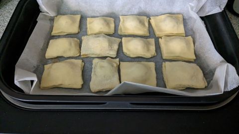 Tiefe Wanne von Hei&szlig;luftfritteuse mit Backpapier auslegen und gef&uuml;llte P&auml;ckchen hineingeben.