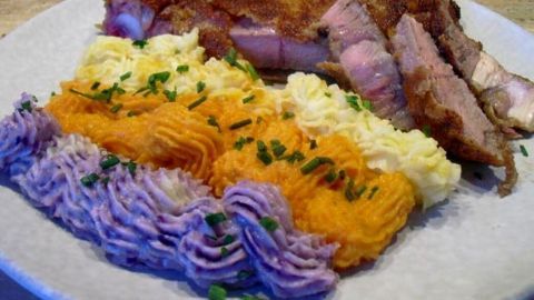 Kalbskottlet auf dem Teller neben buntem Kartoffelpüree in verschiedenen Farben, garniert mit frischem Schnittlauch.