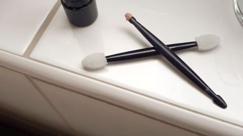 Ein fast leerer Lippenstift und zwei Applikatoren liegen auf einer hellen Oberfläche neben einem Heizkörper.