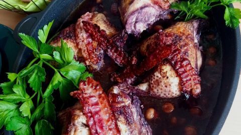 Zart geschmortem Hähnchen in Rotwein, in einer Pfanne angerichtet mit Petersilie und knusprigem Speck, umgeben von Brot.