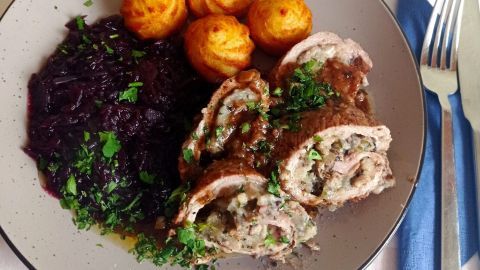 Zarte Involtini vom Kalb auf einem Teller, begleitet von Kartoffeln, Rotkohl und frischen Kräutern.