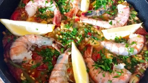Eine Pfanne mit frisch zubereiteter Paella, reich garniert mit Meeresfrüchten, Zitronenscheiben und frischem Gemüse.
