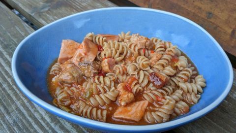Eine Schüssel mit Pfundstopf aus gedrehten Nudeln, Fleisch und Tomatensauce steht auf einer Holzoberfläche.