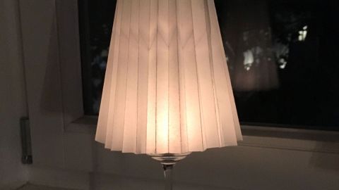 Ein Windlicht aus einem Weinglas strahlt warmes Licht aus und steht auf einem Fensterbrett in der Dunkelheit.