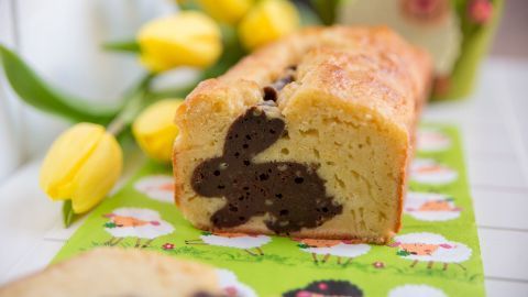 Ein Hasenkuchen steht auf einem bunten, frühlingshaften Tisch mit gelben Tulpen im Hintergrund, die die Osterstimmung unterstreichen.