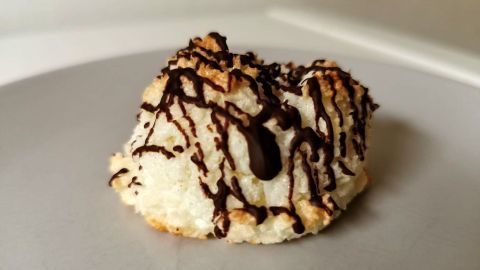 Eine Kokosmakrone ohne Oblaten liegt auf einem weißen Teller, mit einem dekorativen Schokoladenguss überzogen.