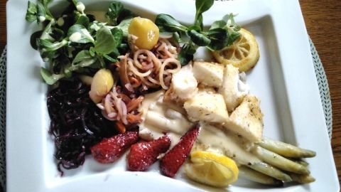Ein gebratener Heilbutt liegt auf Karottenspaghetti, umgeben von frischem Salat und Zitronenscheiben in einer eleganten Anrichtung.