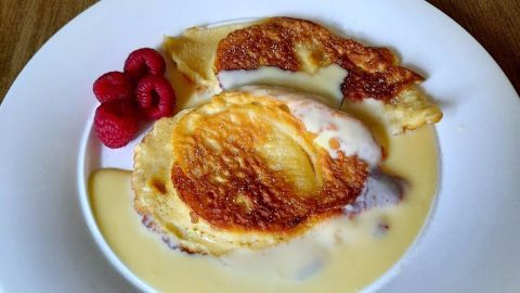 Apfelküchlein liegen auf einem Teller, umgeben von Vanillesoße und garniert mit frischen Himbeeren.