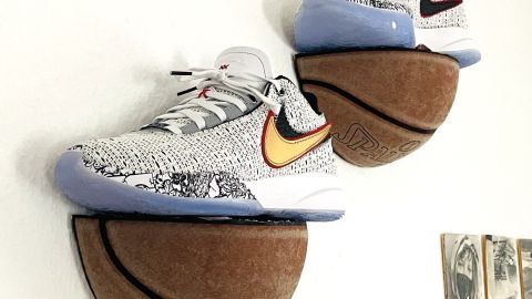 Zwei Basketballschuhe hängen an einer Wand, auf Halterungen aus Basketballen, in einem minimalistischen Raum.