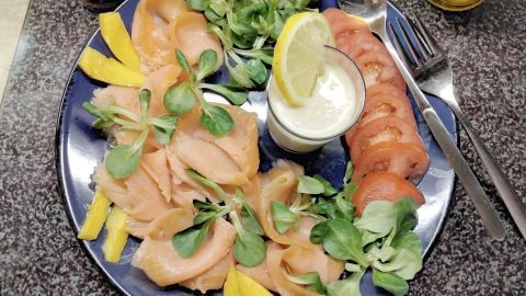 Zartes Räucherlachsfilet liegt zusammen mit frischen Tomatenscheiben, Mango und einem Meerrettich-Dressing auf einem Teller.