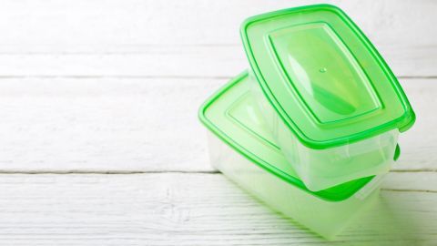 Transparente Tupperware mit grünen Deckeln steht auf einem hellen Holztisch, bereit zur Reinigung von Verfärbungen.