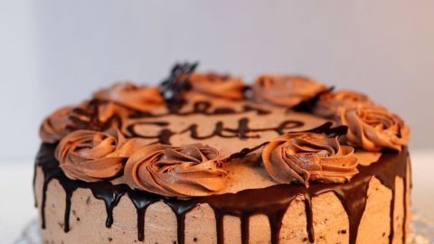 Eine Schokoladensahnetorte steht auf einem silbernen Kuchenständer, dekoriert mit Schokoladenglasur und Sahnerosen.